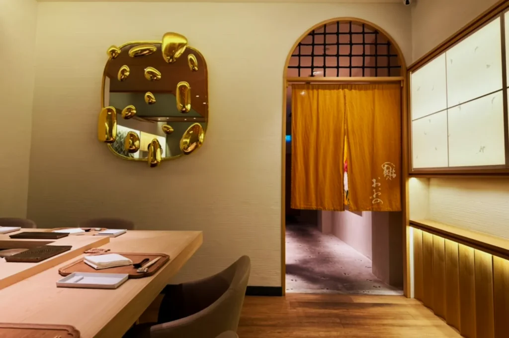 Sophisticated dining room with warm lighting. Features a wooden table set, golden abstract wall art, and a yellow curtain in an arched doorway. Cozy ambiance.