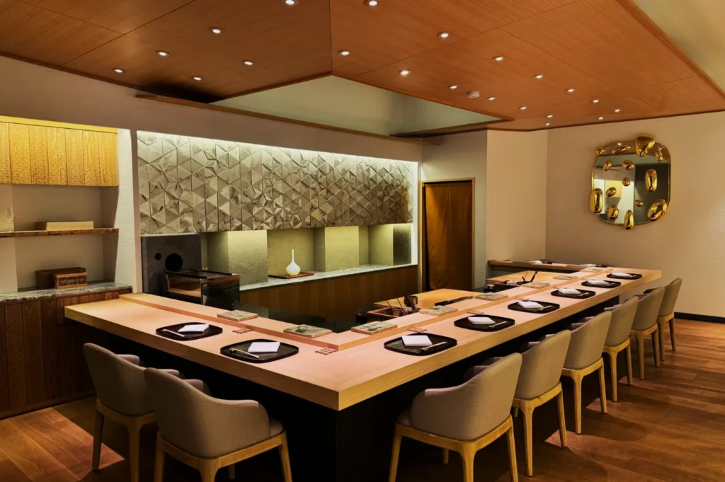 Modern sushi restaurant interior with a U-shaped wooden counter, cushioned chairs, geometric wall art, and elegant, minimalist decor.