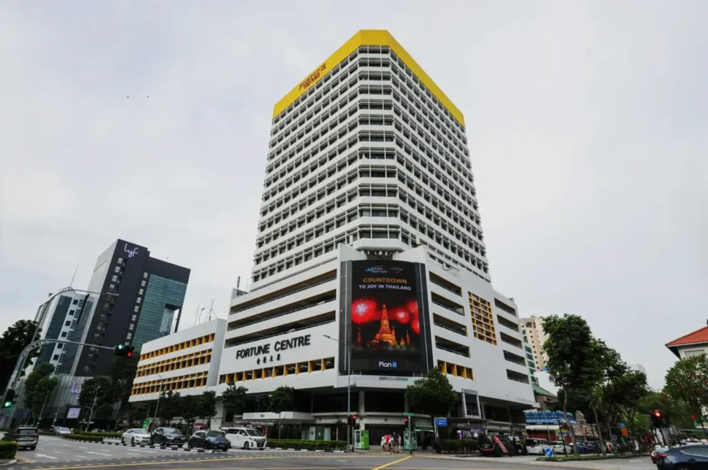A large, multi-story building labeled "Fortune Centre" dominates the scene, featuring a digital billboard on the facade. Nearby buildings and a busy street are visible.
