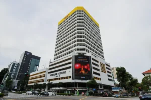 A large, multi-story building labeled "Fortune Centre" dominates the scene, featuring a digital billboard on the facade. Nearby buildings and a busy street are visible.