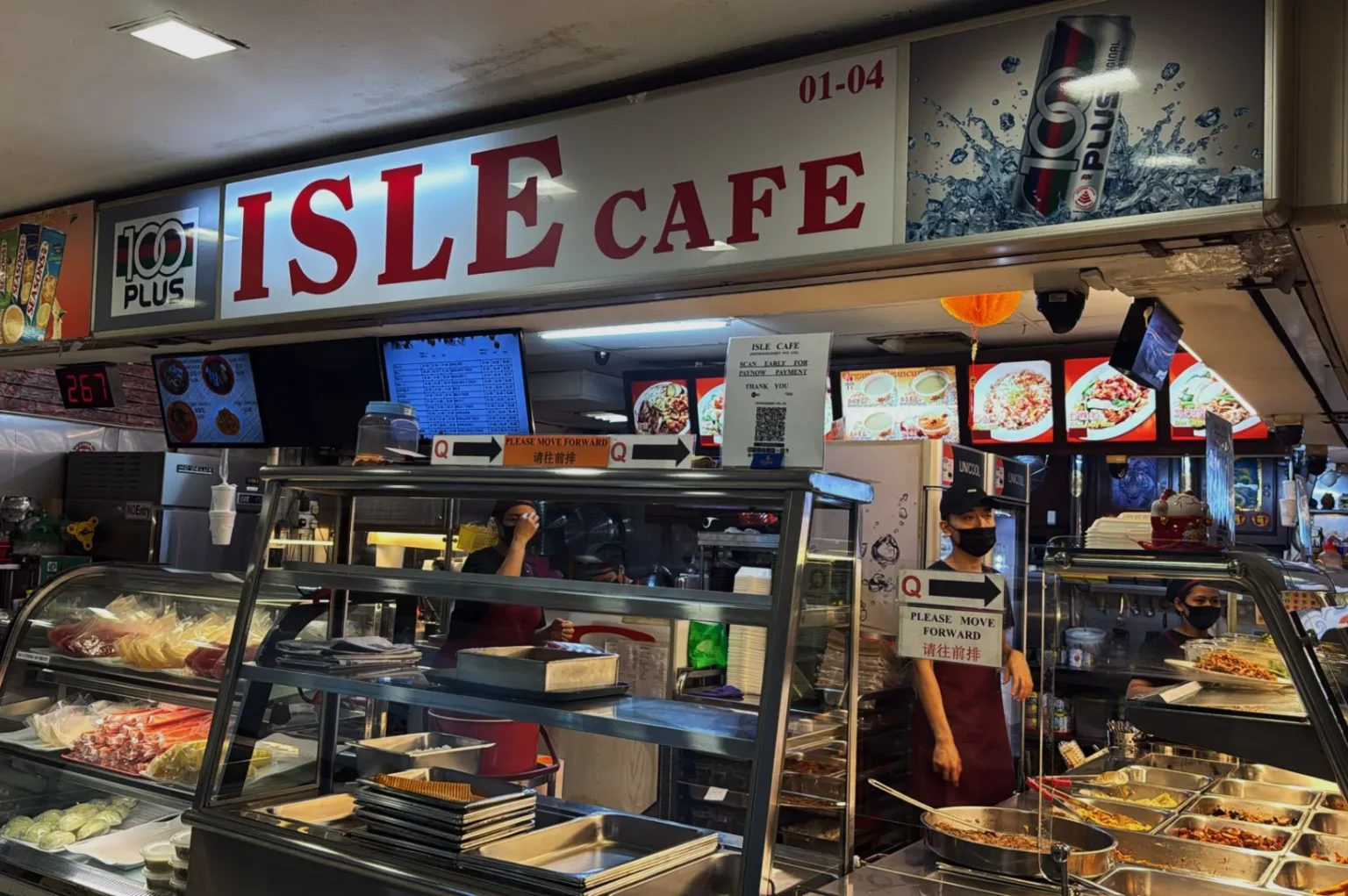 ISLE Cafe counter in a food court, with a variety of dishes displayed. A masked staff member serves food, creating a busy and inviting scene.