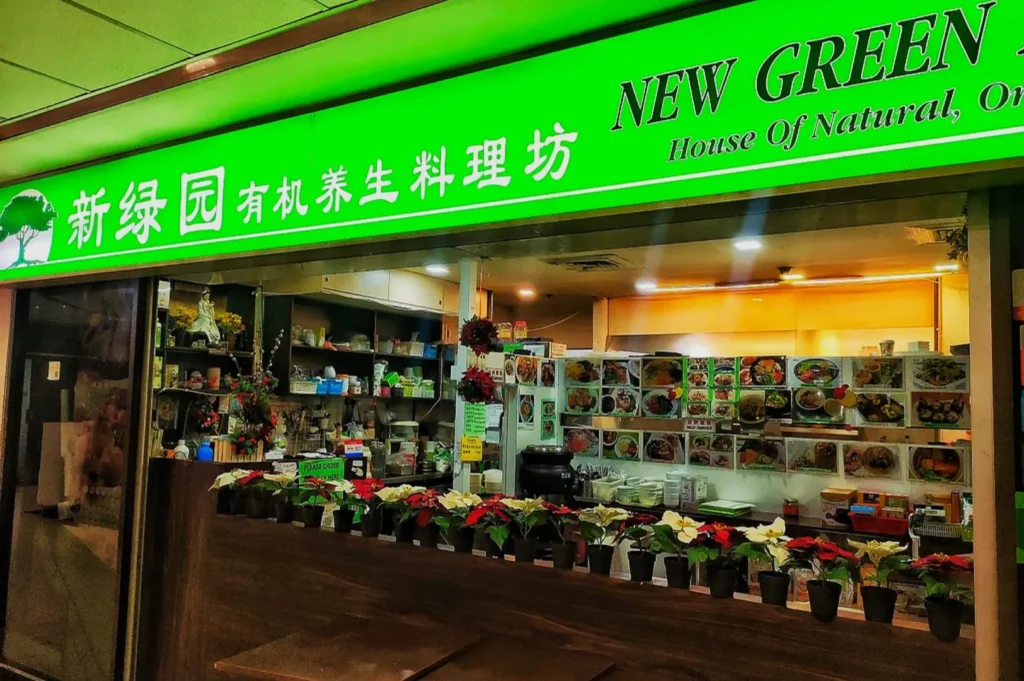 Bright green storefront labeled "New Green", featuring organic dishes. Potted plants line the counter, adding a fresh feel to the inviting space.