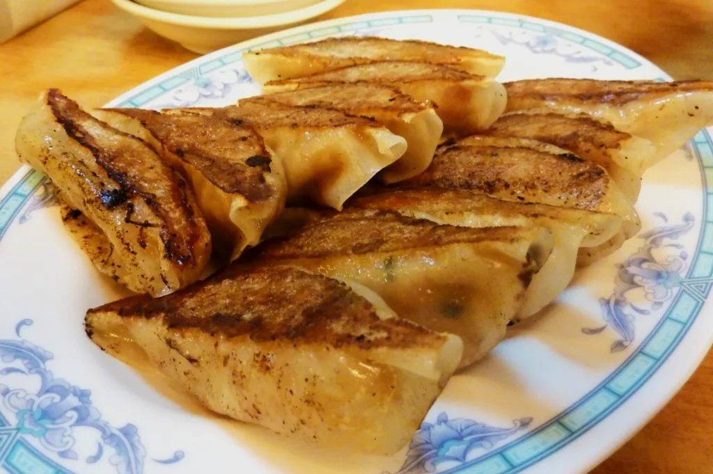 A plate of golden-brown pan-fried dumplings on a decorative dish. The dumplings are crispy on one side, conveying a fresh and appetizing look.