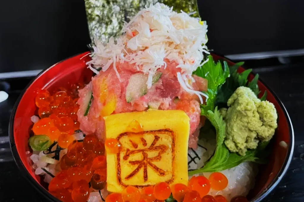A colorful Japanese sashimi bowl with rich toppings, including salmon roe, grated crab meat, yellow tamago with a symbol, wasabi, and fresh greens.