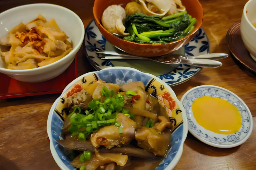 A vibrant meal featuring braised pork with scallions, a bowl of mixed noodles and vegetables, and pickled radishes, accompanied by a small dish of sauce.