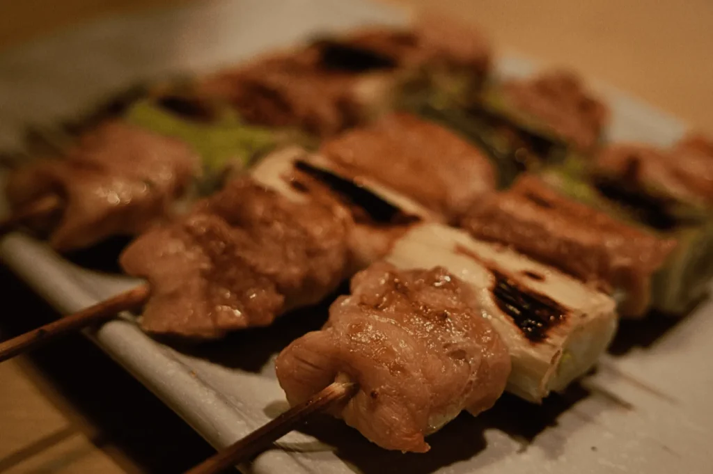 Close-up of grilled chicken skewers on a white plate. Juicy, golden-brown meat is interspersed with charred green onions, creating a savory presentation.