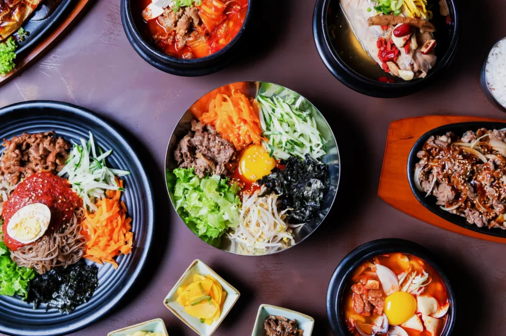 An array of Korean dishes on a table, featuring colorful bibimbap, kimchi stew, and bulgogi. Small side dishes enhance the vibrant, appetizing scene.