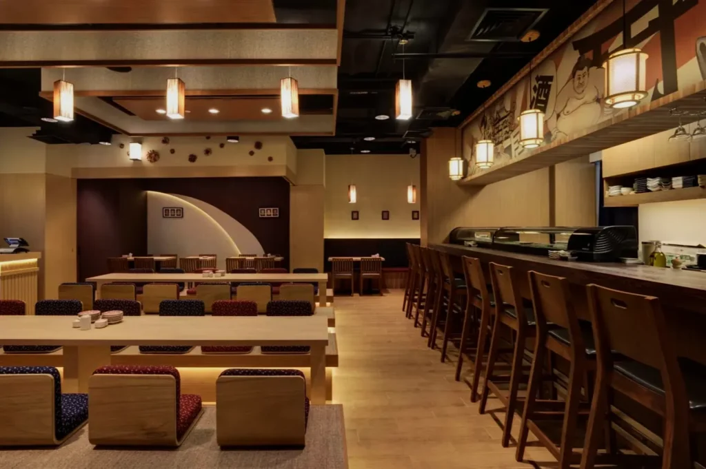 Modern Japanese restaurant interior, featuring wooden tables, cushioned seats, and a sushi bar. Ambient lighting creates a warm, inviting atmosphere.