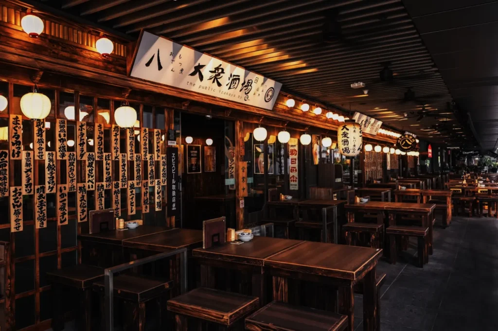 Cozy Japanese restaurant at dusk, wooden tables and lanterns line the sidewalk. Warm lighting and traditional signs create an inviting, nostalgic atmosphere.