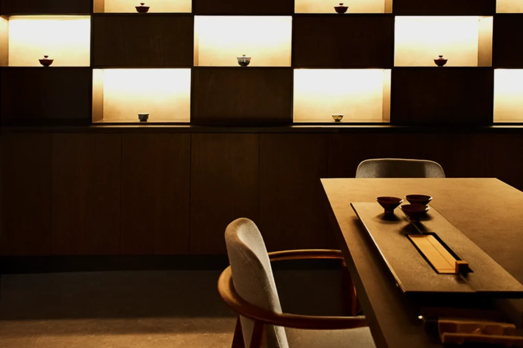 A row of white ceramic cups on dark saucers is aligned on a sunlit table. Gentle steam rises from them, creating a calm and serene atmosphere.
