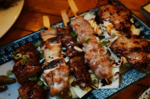A platter of assorted grilled skewers, featuring savory chicken and beef atop shredded cabbage, garnished with green onions on a decorative plate.