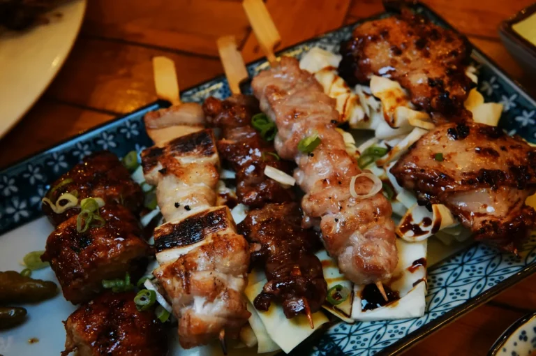 A platter of assorted grilled skewers, featuring savory chicken and beef atop shredded cabbage, garnished with green onions on a decorative plate.