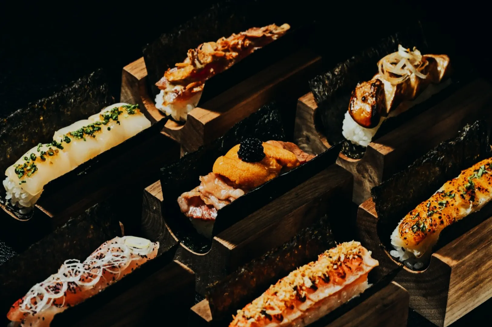 A vibrant array of sushi pieces elegantly presented on wooden stands. Each sushi is uniquely topped with ingredients like herbs and sauces, showcasing artistry and flavor.