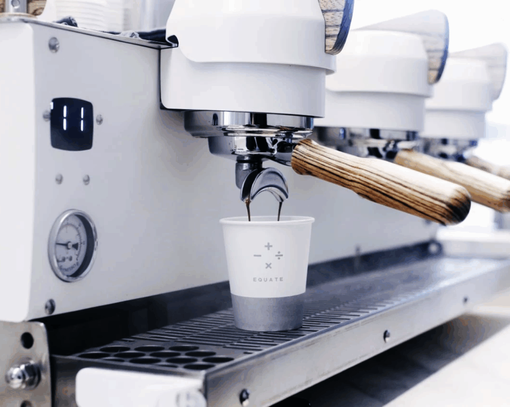 Beyond the Orchard Road : A barista at Equate Coffee is brewing a fresh cup with no whipped cream using a sleek espresso machine, capturing the warm ambience and artisanal coffee-making process.