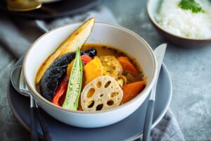Sapporo Soup Curry in SG : A steaming bowl of Hokkaido-style soup curry filled with vibrant vegetables and a tender chicken leg, served alongside fluffy white rice for a balanced and comforting meal.