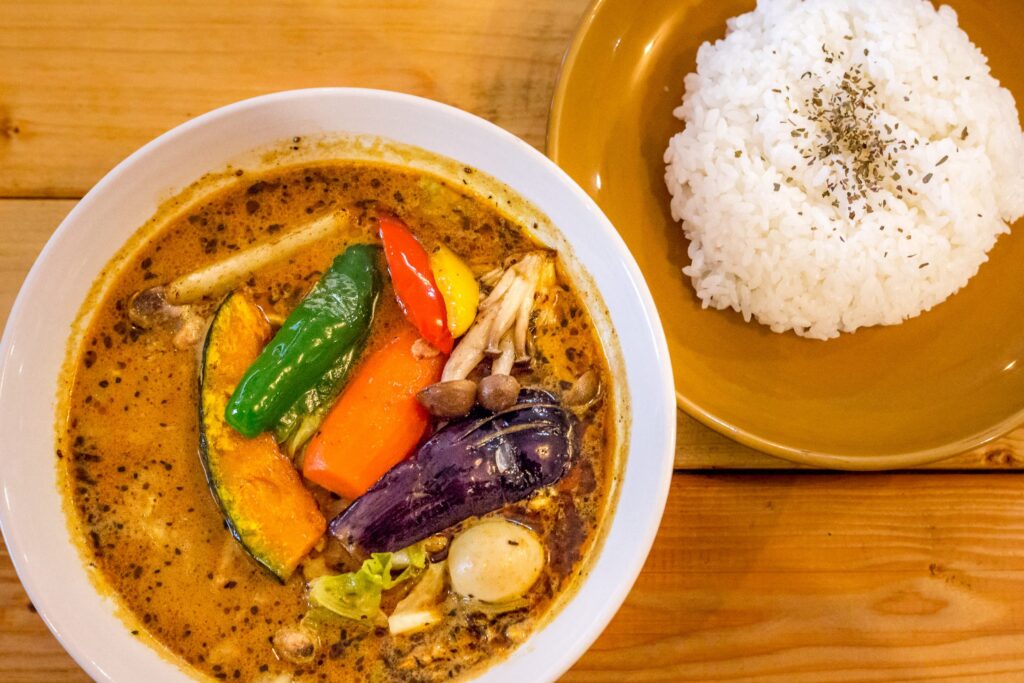 Sapporo Soup Curry in SG : Golden, spiced broth brimming with aromatic flavours and colourful toppings—carrots, bell peppers, and eggplant—capturing the warmth of Sapporo’s signature dish.