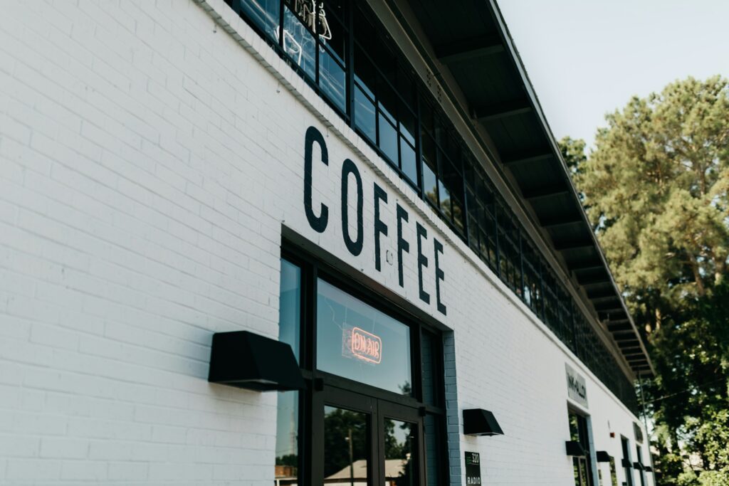Best Coffee in SG : Exterior view of a charming café in Singapore with outdoor seating, surrounded by lush greenery and soft morning light, inviting coffee lovers to unwind with a perfectly brewed cup.