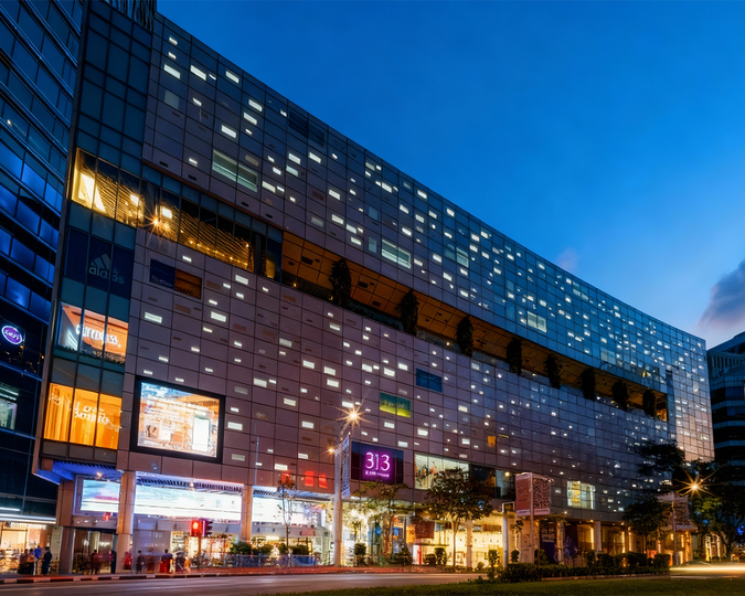 Beyond the Orchard Road : A night-time view of 313 Somerset Mall in Singapore, illuminated with vibrant exterior lights that highlight its modern architecture, bustling atmosphere and the lively street scene surrounding the entrance.