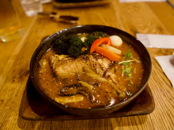 Sapporo Soup Curry in SG : A beautifully presented bowl of Hokkaido soup curry on a wooden table, the rich aroma of spices rising from the broth—an authentic taste of Sapporo’s culinary soul