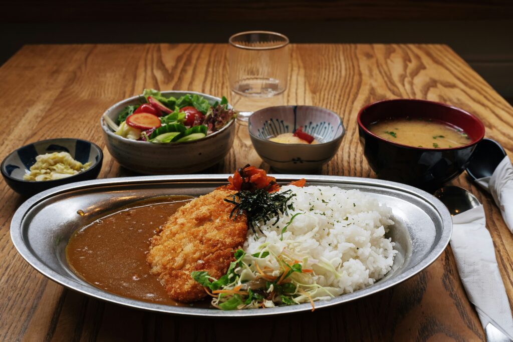 A plate of Japanese curry served with steamed rice and assorted side dishes on a wooden table.