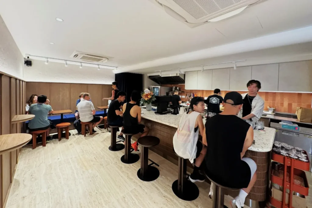 People sitting at a modern café counter and tables, chatting and enjoying drinks. The atmosphere is relaxed and social, with soft lighting.