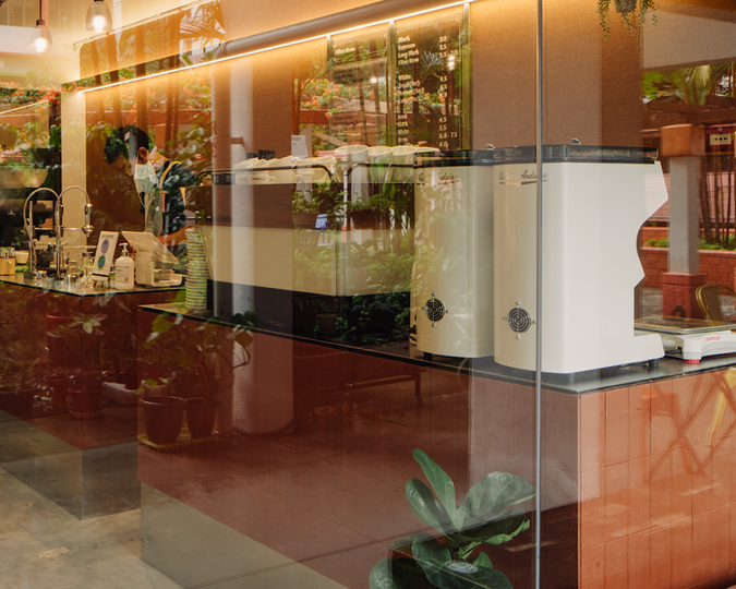 The interior view of Nylon Coffee Roasters’ café bar, showcasing its minimalist setup, warm lighting, and baristas preparing drinks behind the counter.