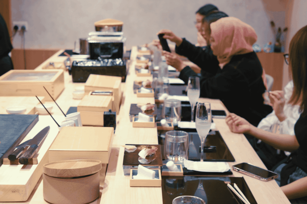 A group of diners seated at a minimalist sushi counter, each with a tray of omakase delicacies and drinks—capturing a quiet moment of appreciation and ritual in Singapore’s refined Sushi Masa by Ki-setsu.