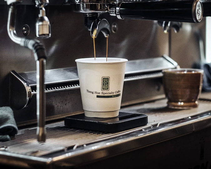A barista at Tiong Hoe Specialty Coffee carefully operating a coffee machine, with fresh espresso pouring smoothly into a cup below