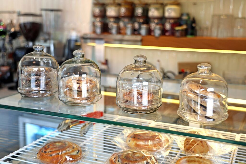 The image depicts a small, cozy dessert shop filled with affordable sweet treats, including colorful pastries and cakes, inviting dessert lovers to browse and enjoy. Comfortable chairs are arranged around the space, creating a welcoming atmosphere for friends to share a matcha latte or black coffee while indulging in delicious desserts.
