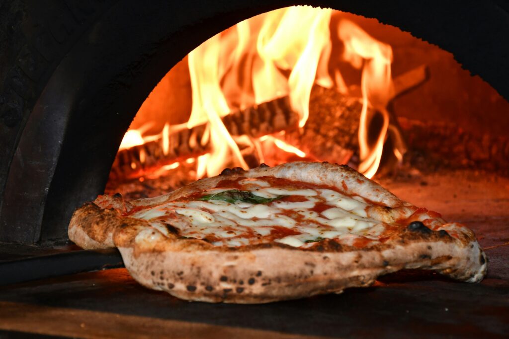 A traditional wood-fired pizza oven with vibrant flames is shown, baking a fresh pizza made from quality pizza dough. This image captures the essence of pizzerias like l'antica pizzeria da michele, where diners can enjoy the perfect slice of Italy's culinary tradition.