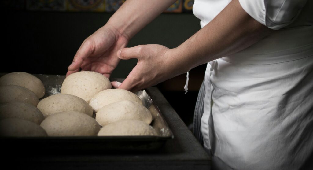 A chef skillfully stretching and preparing pizza dough in a bustling kitchen, showcasing the craftsmanship and passion behind authentic Italian pizza-making