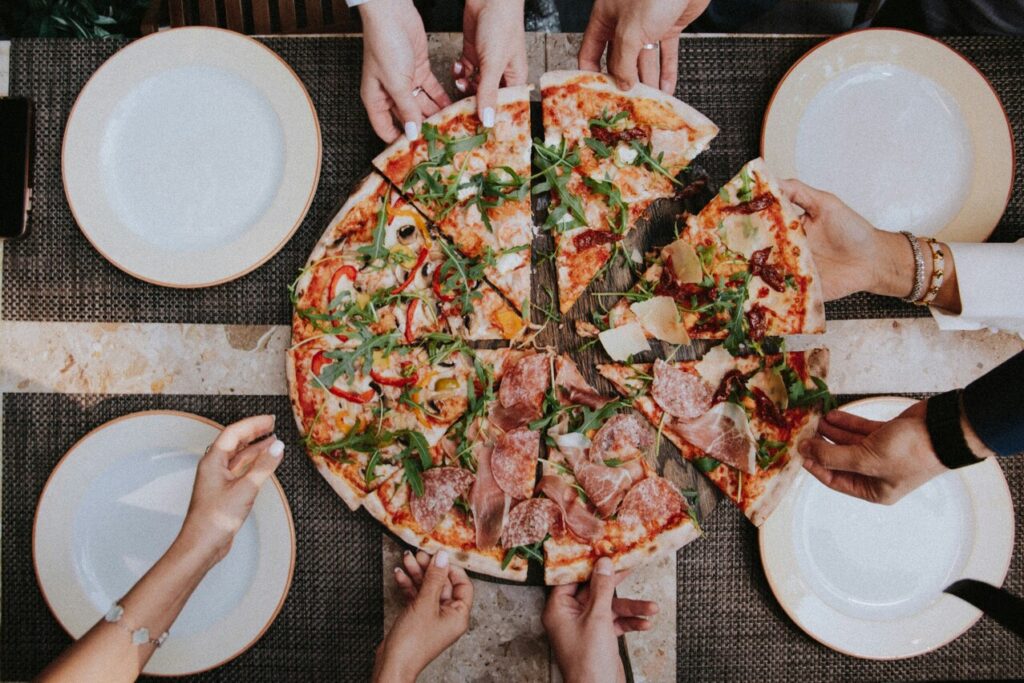 Several hands reaching for slices of pizza on a table, each pulling away cheesy, delicious pieces, capturing the communal and fun experience of sharing a meal