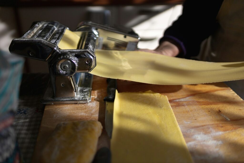 In a bustling restaurant kitchen, skilled hands expertly roll and shape fresh pasta dough, embodying the art of authentic Italian food. The scene captures the essence of handmade pasta preparation, highlighting the dedication to traditional pasta shapes that are a hallmark of Italian cuisine.