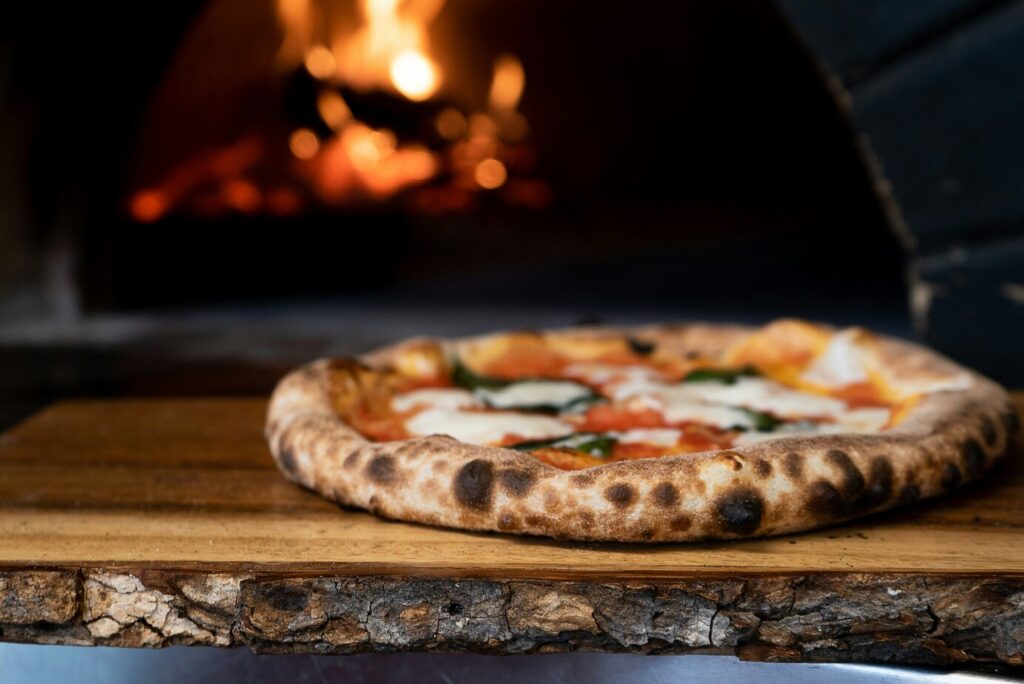 A freshly baked pizza sitting inside a rustic wooden oven, with golden melted cheese and perfectly cooked crust visible under the warm oven light.
