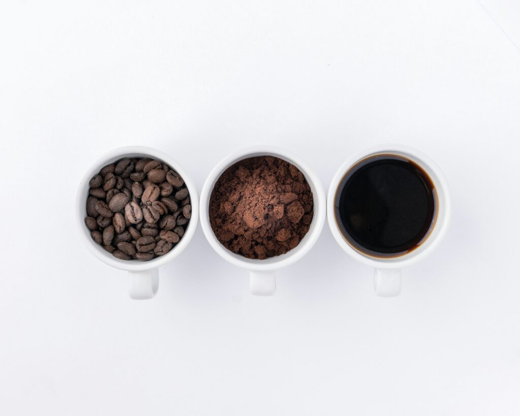 A rustic arrangement featuring a cup of brewed coffee surrounded by fresh coffee beans and finely ground coffee powder, highlighting the journey from bean to cup