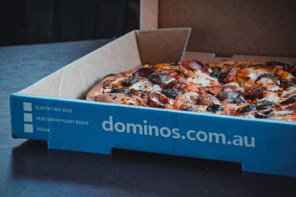 An open Domino’s pizza box revealing a freshly baked pizza inside, with perfectly arranged toppings and a golden-brown crust ready to be enjoyed.