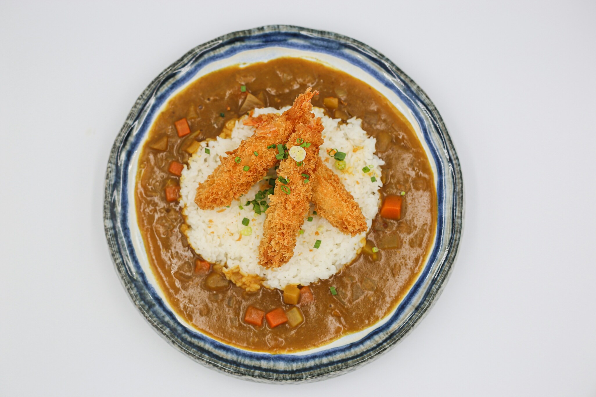 A steaming bowl of Japanese curry rice features a golden katsu cutlet resting atop fluffy white rice, accompanied by rich curry sauce, creating a satisfying meal that highlights the delicious flavors of Japanese cuisine. The dish is garnished with vibrant vegetables, adding to its hearty appeal.