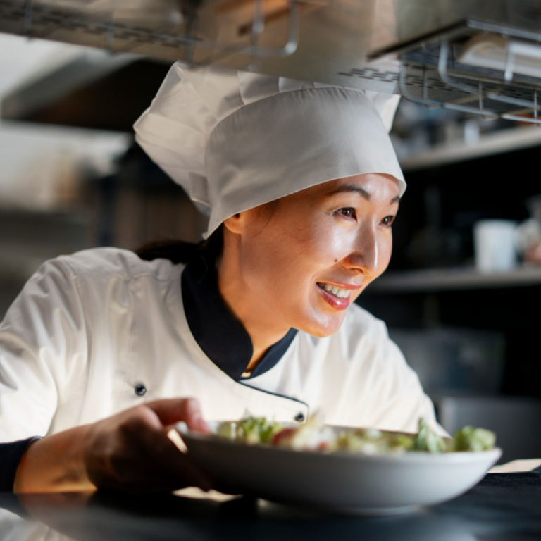 A woman chef gently placing a finished dish on the table, reflecting pride, craftsmanship, and attention to detail after cooking.