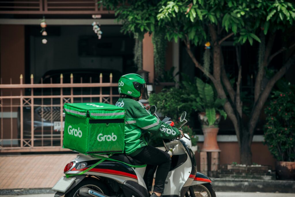 A Grab delivery rider on a motorcycle transporting festive food orders, representing fast and reliable delivery during the busy Chinese New Year season.
