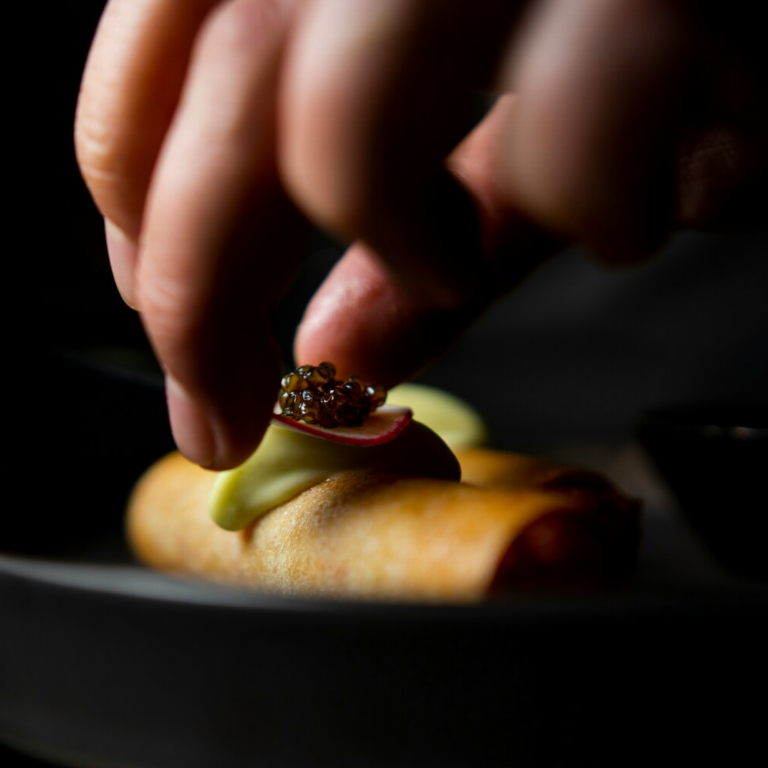 A close-up of a hand placing food onto a plate, capturing the final touch that completes the presentation of the dish.