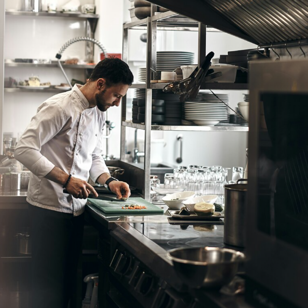 A chef actively cooking in a restaurant kitchen, focused and immersed in the process of preparing a carefully crafted meal.