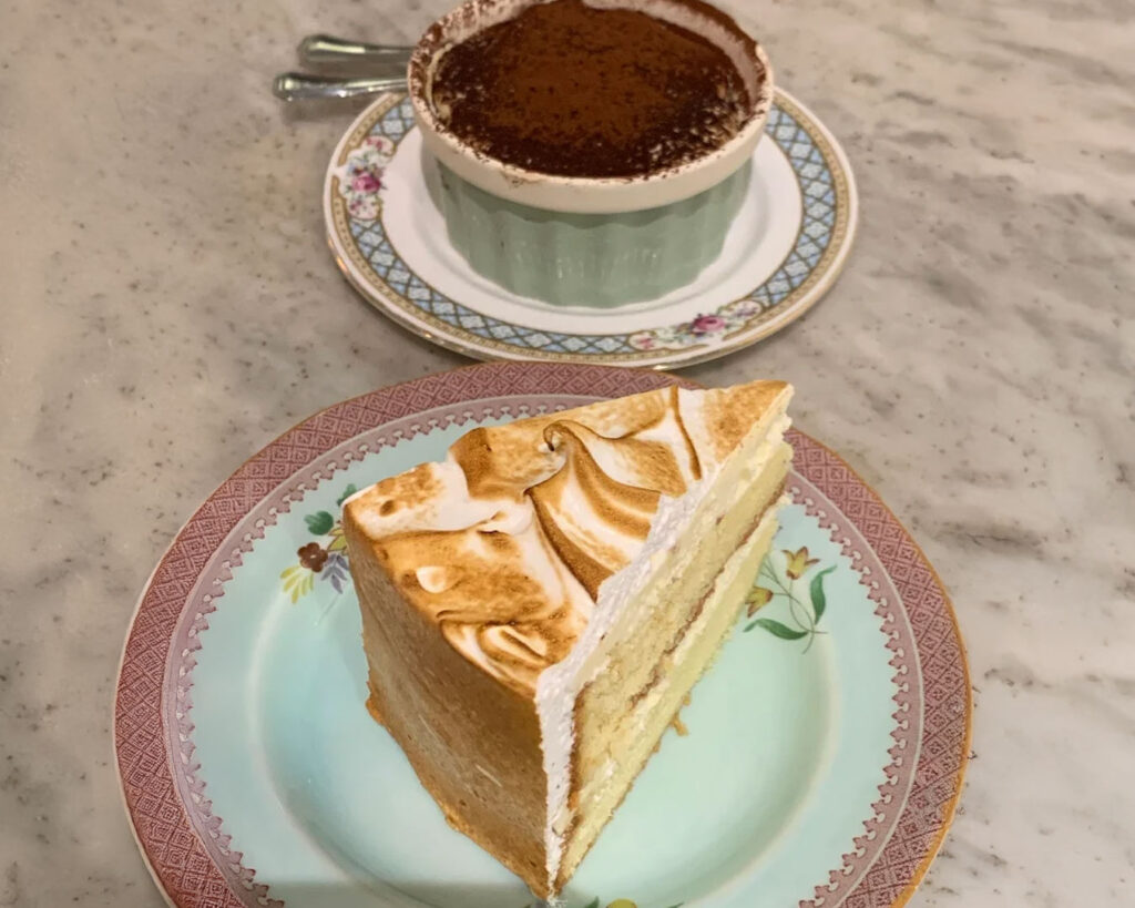 A passionfruit tart topped with toasted meringue peaks, resting on a plate in Carpenter and Cook’s vintage-style café setting with warm wooden furniture.