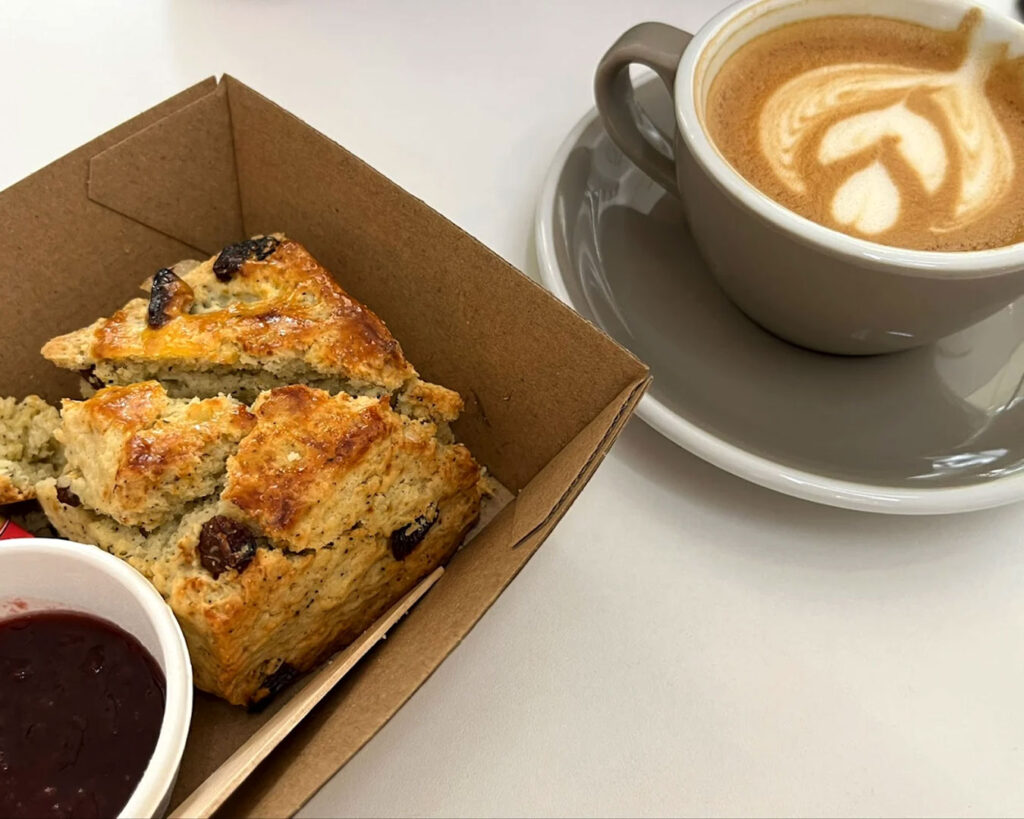 A cup of freshly brewed coffee paired with a plated dessert, presented on a wooden table in Glyph Supply Co.’s modern café interior with warm tones and natural light.
