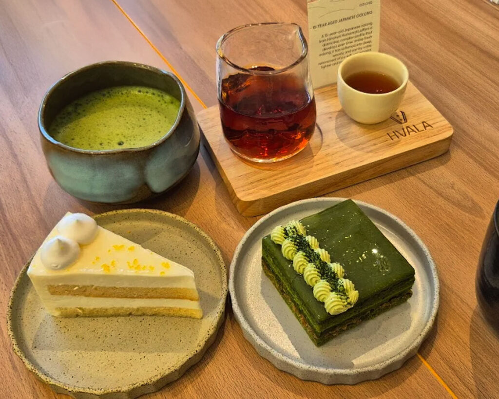 A slice of matcha goma cake with a smooth green tea sponge and nutty sesame layers, served neatly on a plate in Hvala’s minimalist café setting with soft lighting.