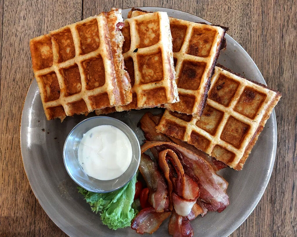 A golden waffle served with toppings on a plate, photographed on a marble table inside Nassim Hill Bakery Bistro Bar with an elegant café atmosphere.