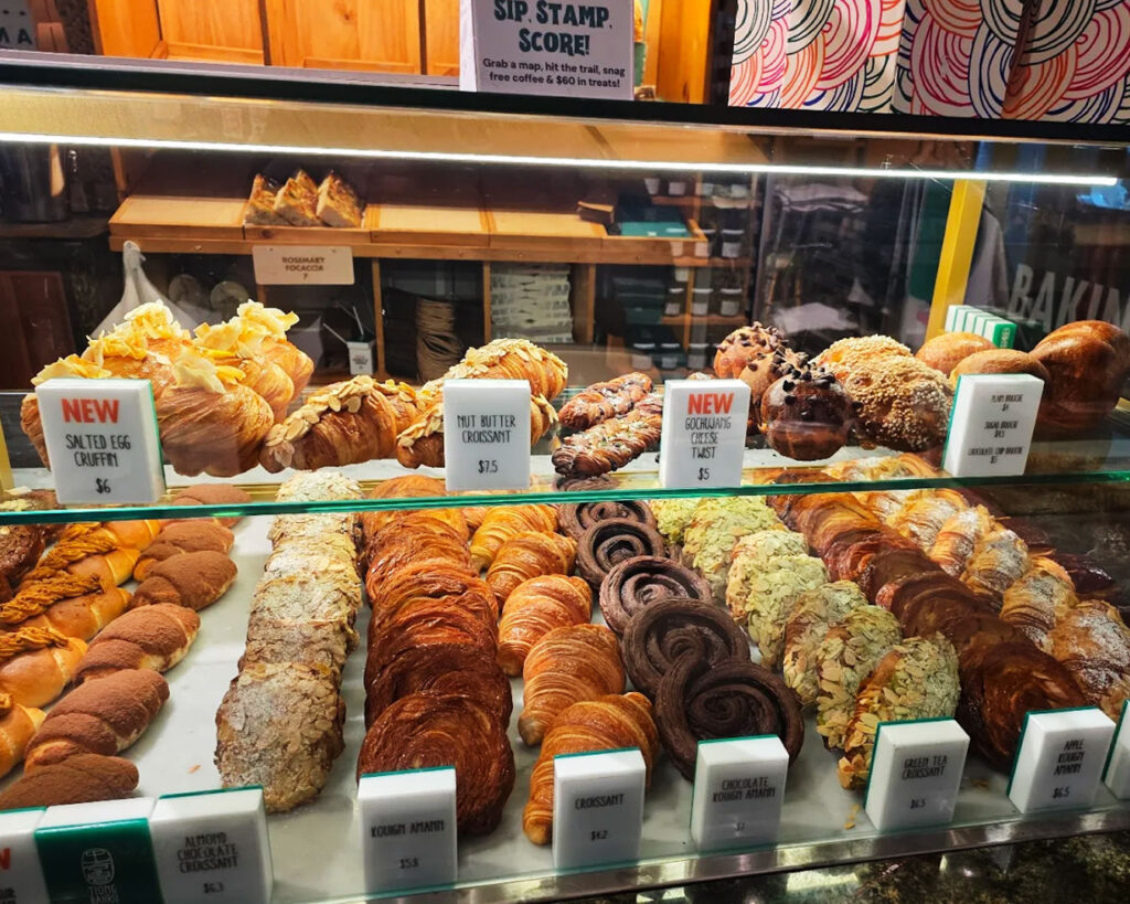 An assortment of pastries including croissants and danishes arranged on ceramic plates, set against the cosy interior of Tiong Bahru Bakery with shelves and warm lighting.