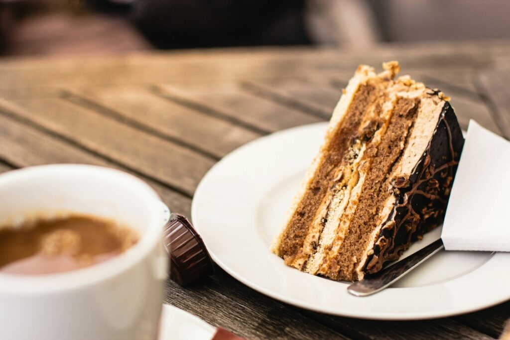 A delicate slice of cake served on a ceramic plate inside a cosy café, with soft natural light highlighting its layers and creating a warm, inviting atmosphere