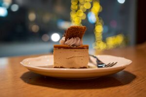 A delicate slice of cake served on a ceramic plate inside a cosy café, with soft natural light highlighting its layers and creating a warm, inviting atmosphere.