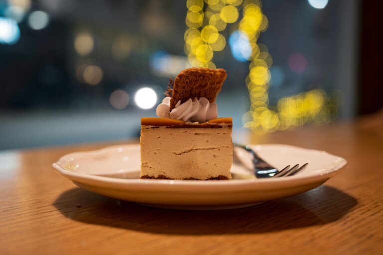 A delicate slice of cake served on a ceramic plate inside a cosy café, with soft natural light highlighting its layers and creating a warm, inviting atmosphere.