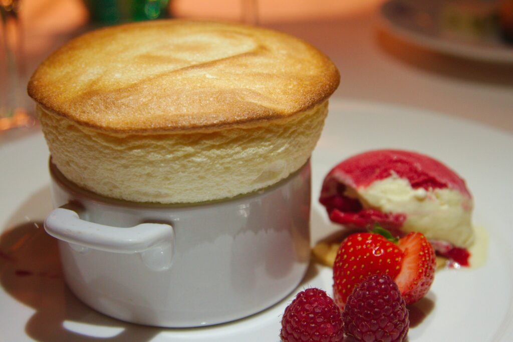 A perfectly risen soufflé with a golden, airy top, lightly dusted with sugar. The delicate texture captures a balance of warmth and fluffiness, showcasing the dessert’s classic French elegance